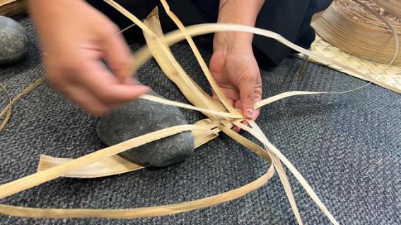 This is a close-up picture of hands weaving some flax on a mat