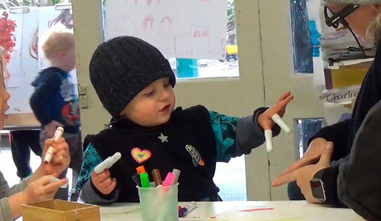 This is a photo of a child next to a tabletop with pen lids on his fingers