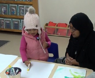 This is a photo of a pre-schooler showing her teacher a drawing