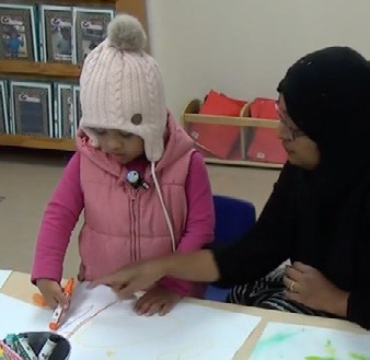 This is a photo of a pre-schooler showing her teacher a drawing. The teacher is pointing to the drawing