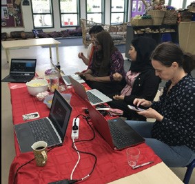 A photo of four teachers in front of laptops. Some of them are also looking at their mobile phones