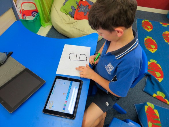 This is a photo of a boy at a table, writing on a small white board with an iPad next to it