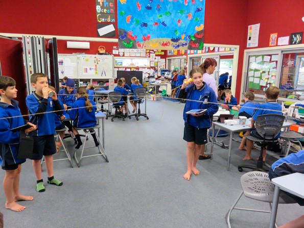 This photo shows four students talking into, or listening to, cans connected by string