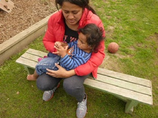 This is another picture of a woman sitting on a bench, holding a child in her arms