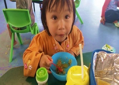 This is a close up of a child using a spoon to eat food from a bowl