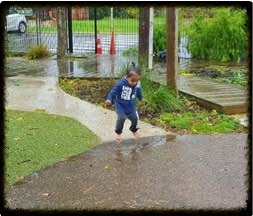 This is a long shot of a child jumping in a puddle