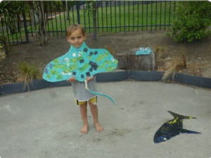 This is a picture of a child standing next to the stingray they'd drawn on some concrete outside