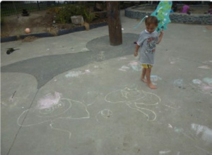 This is a picture of a child standing next to the stingray they'd drawn in chalk on some concrete outside