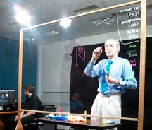 A photo of a man writing (in white) on some glass