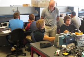 This is a photo of a lecturer standing beside several students working at benches with equipment