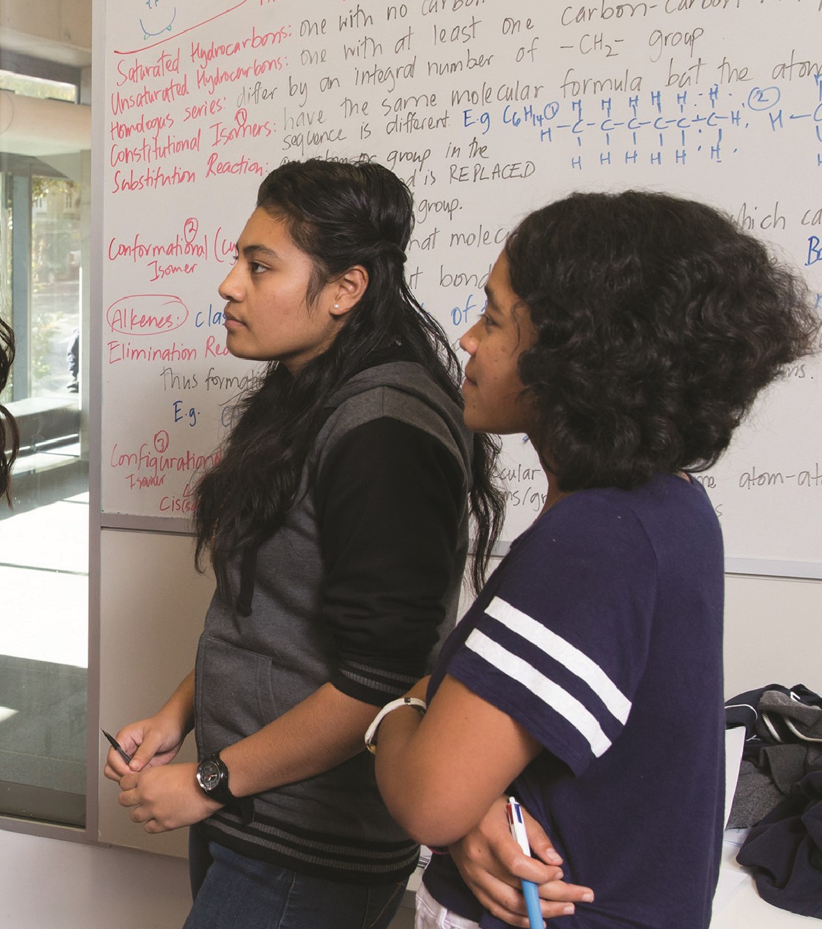 A photo, presumably of two students, standing side on to a whiteboard. They are both holding pens