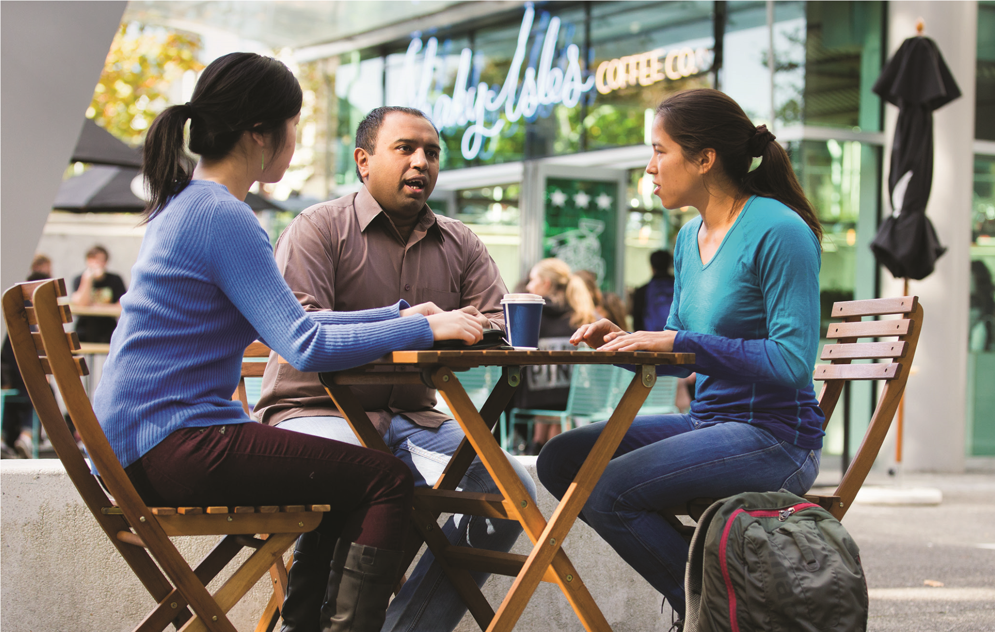 A photo of a man and two women sitting at a table outside a cafe