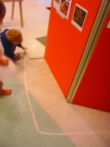 A picture of a child drawing a chalk mark on the floor in front of an art exhibit