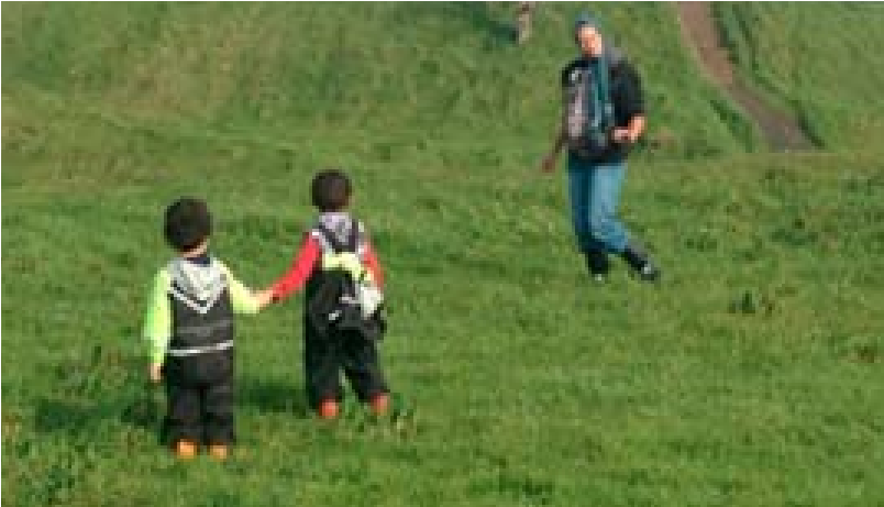 This is a picture of two children holding hands near the bottom of a hill, while an adult walks around in the distance