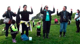 This is a picture of four adults doing what could be a haka. They are outside, and there's children in the picture too