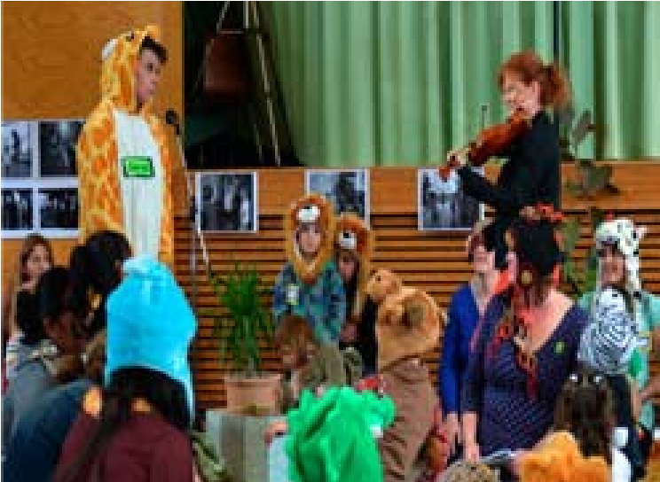 A photo of the children dressed up for the play. An adult is playing a violin next to them