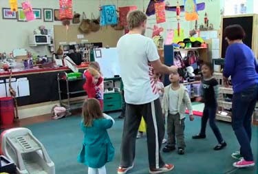 A photo of a man gesturing in front of half a dozen children and the teacher