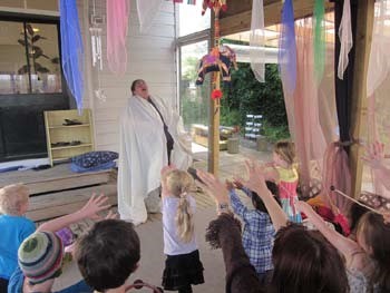 A photo of a teacher standing in front of the children. She's wearing a white sheet