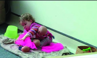 This is a picture of an infant sitting on a mat playing with several dolls