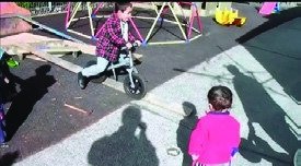 This is a photo of a boy riding a bike and a younger child watching him