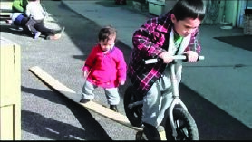 This is another photo of a boy riding a bike and a younger child watching him