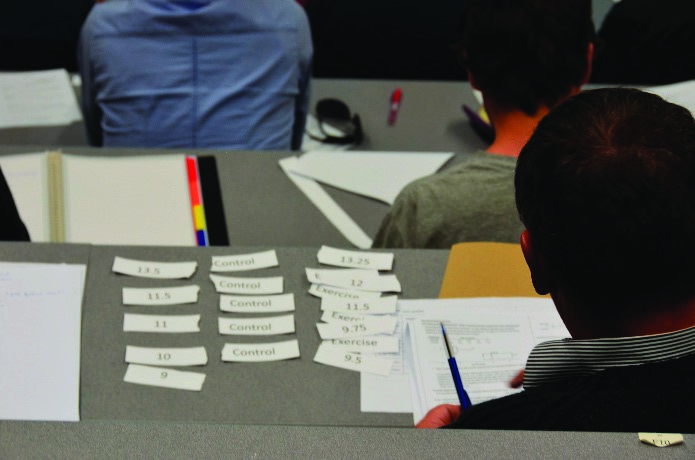 This photo shows a student sitting in a lecture theatre with strips of paper on the bench in front of him