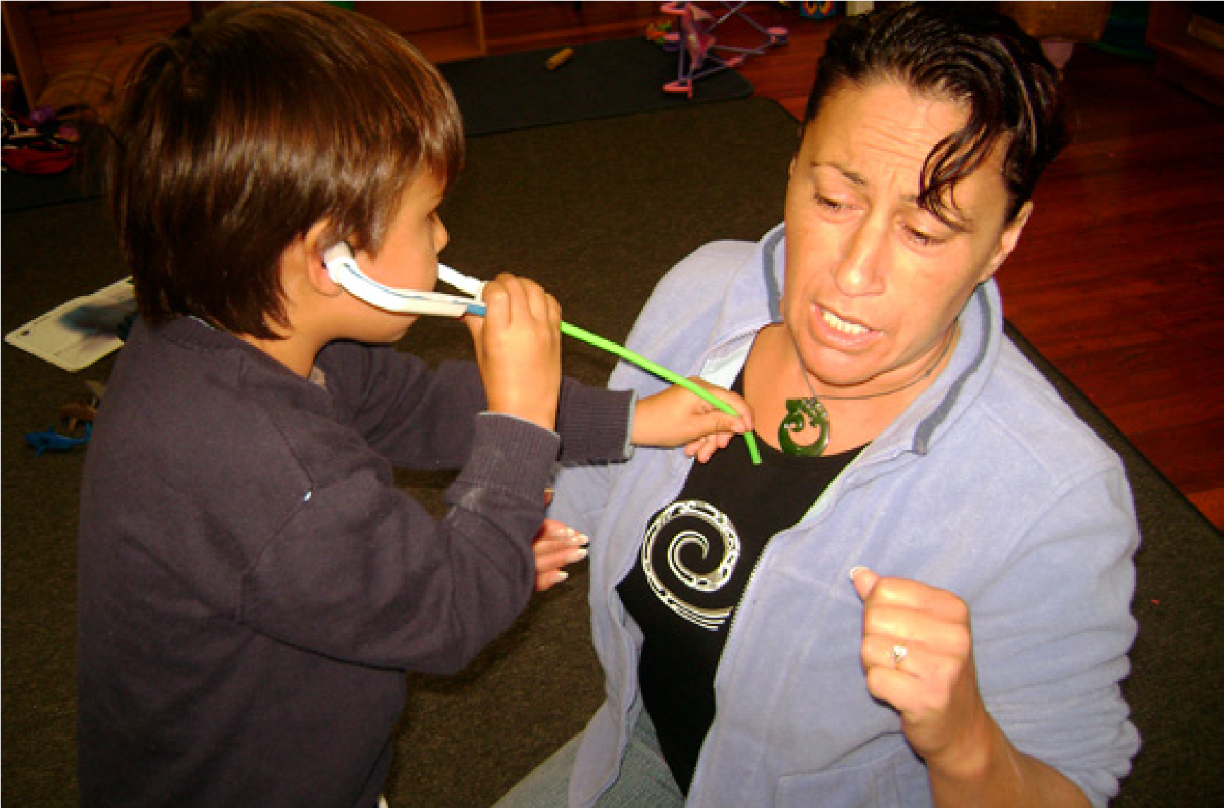 A young boy, holding a stethoscope, hold it to the teacher's chest 