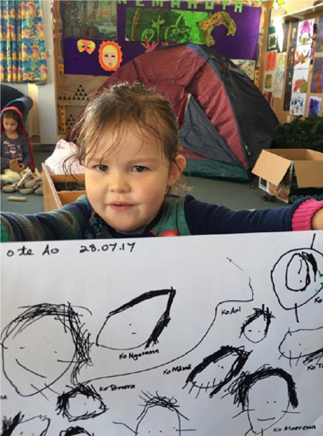 A young girl proudly displaying a large piece of paper, which has her drawings on it