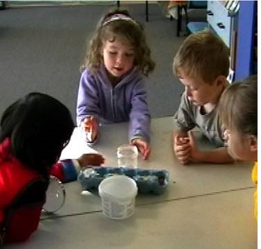 A photo of four children gathered around a table on which there are containers