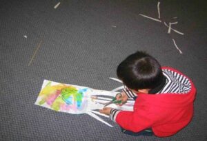 An aerial shot of a child crouched on the floor, making his kite