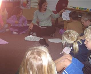 A teacher and students sitting in a circle. The teacher is talking and looking at a piece of paper