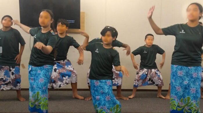 This is a photo of seven students (bus and girls) dancing. They are all wearing black t-shirts with blue skirts. 