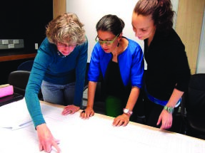 This is a photo of 3 teachers looking at pieces of paper on top of a table