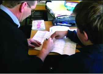 This is a photo of a teacher and a student, sitting together, working on a maths exercise