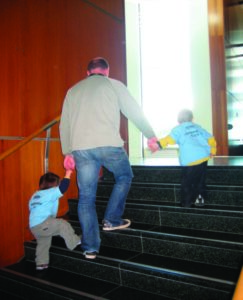 A photo of a man leading, by the hands, two small children up some steps