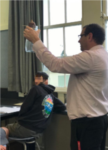 A picture of a teacher holding a jar with a prepared piece of kumara