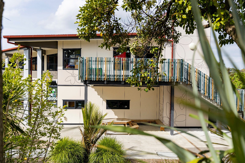 A picture of a two storey classroom, taken from outside. There's foliage in the foreground